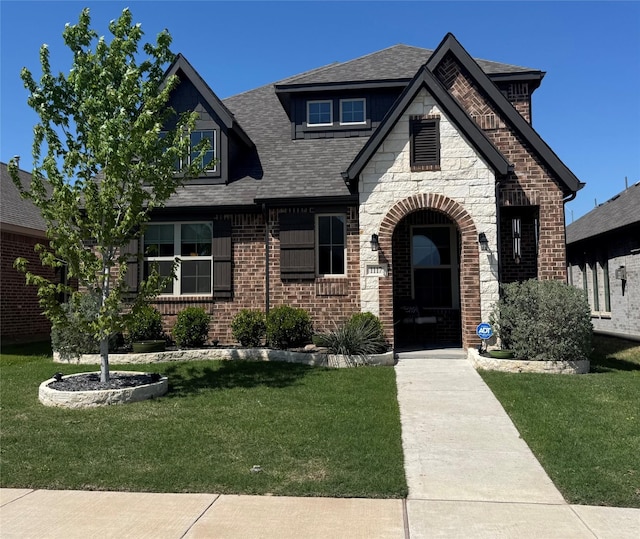 view of front of property featuring a shingled roof, a front yard, and stone siding