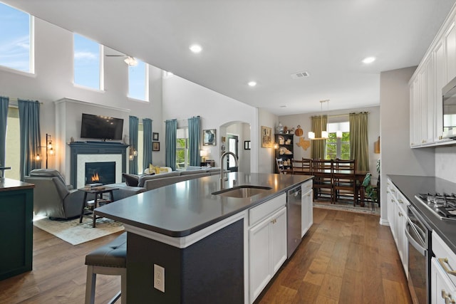 kitchen with dark countertops, dark wood-type flooring, stainless steel appliances, arched walkways, and a sink