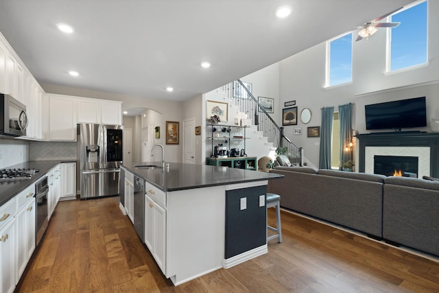 kitchen with a ceiling fan, appliances with stainless steel finishes, a sink, dark countertops, and open floor plan