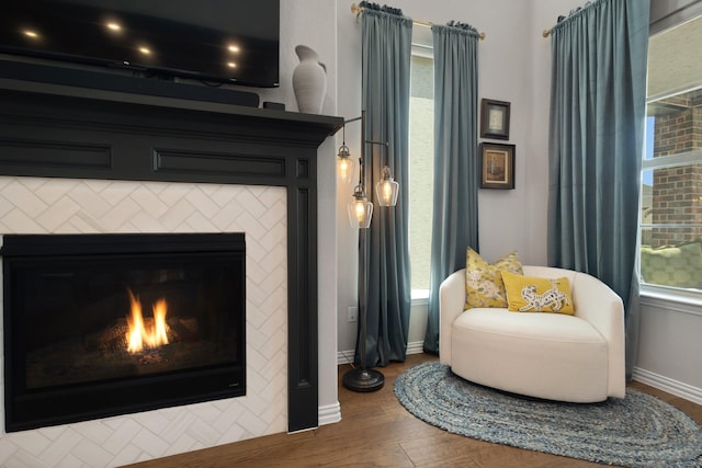 living area with wood finished floors, baseboards, and a warm lit fireplace
