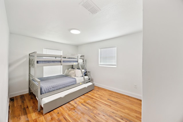 bedroom with visible vents, multiple windows, baseboards, and wood finished floors