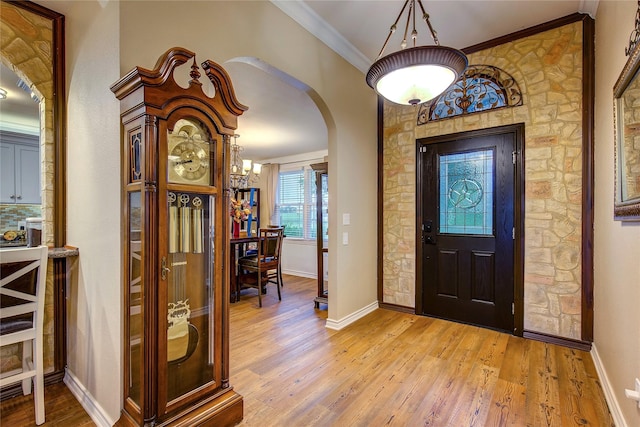 foyer entrance with crown molding, light wood-type flooring, baseboards, and arched walkways