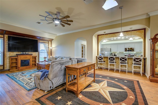 living room featuring light wood-style flooring, a ceiling fan, crown molding, visible vents, and arched walkways