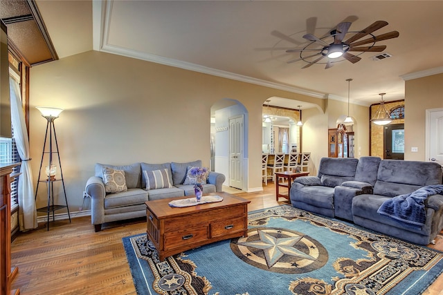 living room featuring wood finished floors, a ceiling fan, visible vents, arched walkways, and ornamental molding