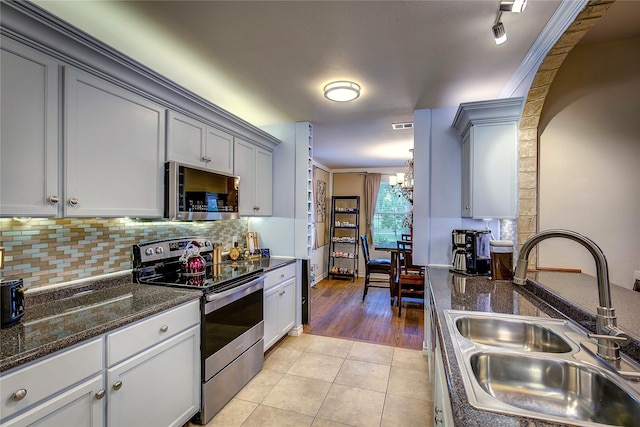 kitchen with a sink, stainless steel appliances, a chandelier, backsplash, and light tile patterned floors