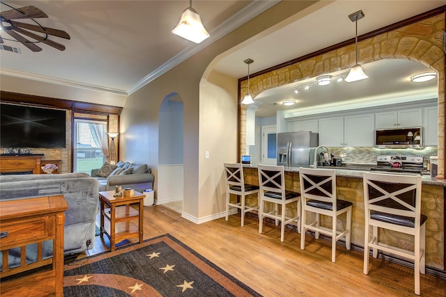 dining room featuring wood finished floors, ornamental molding, visible vents, ceiling fan, and arched walkways
