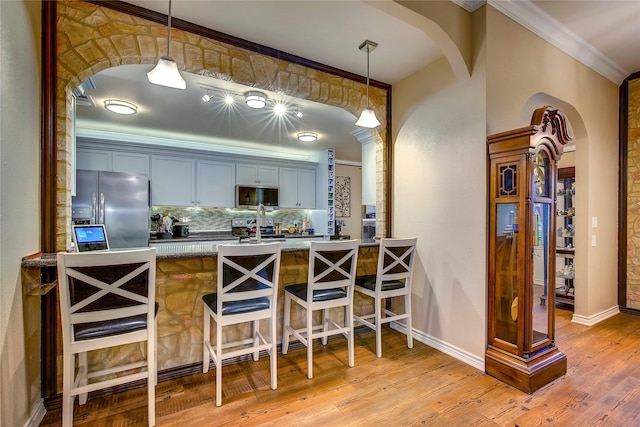 bar with tasteful backsplash, decorative light fixtures, ornamental molding, light wood-type flooring, and appliances with stainless steel finishes