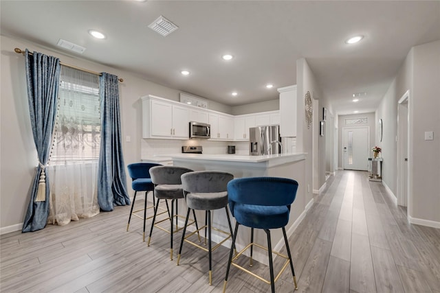 kitchen featuring light wood-type flooring, visible vents, a breakfast bar, and appliances with stainless steel finishes