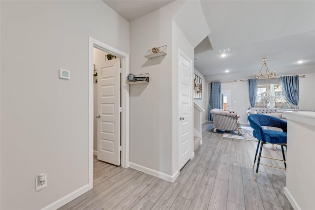 corridor featuring light wood-style floors, an inviting chandelier, baseboards, and recessed lighting