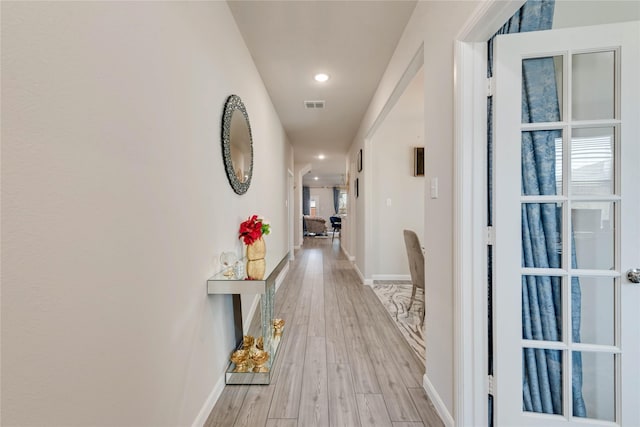 hallway with light wood finished floors, baseboards, visible vents, and recessed lighting