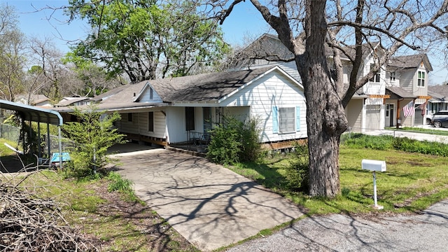 ranch-style home featuring concrete driveway, a shingled roof, a front lawn, and an attached carport