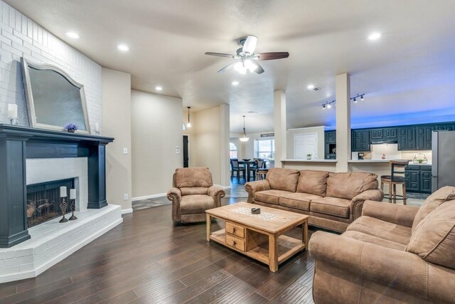 living room featuring baseboards, a brick fireplace, a ceiling fan, recessed lighting, and dark wood-type flooring