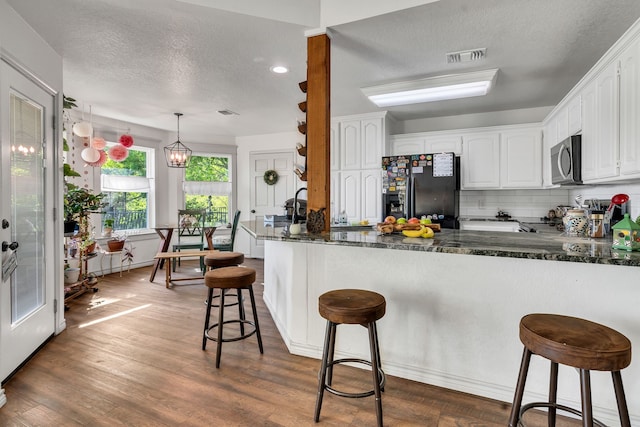 105 Park Trail Pl, Joshua, TX 76058 - kitchen with black fridge with ice dispenser, stainless steel microwave, a textured ceiling, white cabinetry, and a peninsula