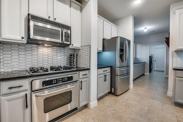 kitchen with stainless steel appliances, washer / dryer, dark stone counters, decorative backsplash, and white cabinetry