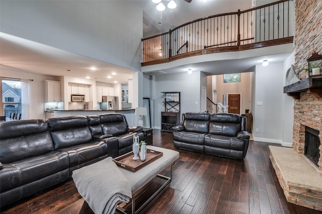 living room with a stone fireplace, a towering ceiling, and dark wood-style floors