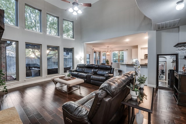 living area with dark wood-style floors, visible vents, baseboards, a towering ceiling, and ceiling fan with notable chandelier