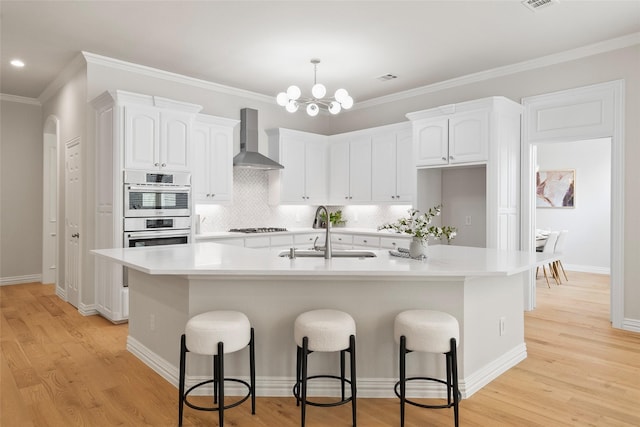 kitchen featuring light wood-style floors, wall chimney exhaust hood, white cabinets, gas cooktop, and a sink