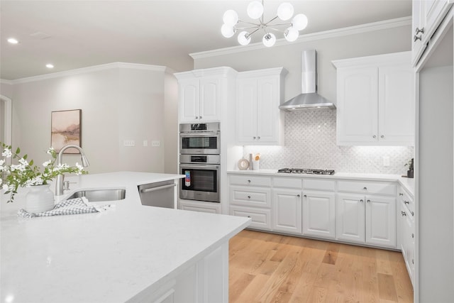 kitchen with wall chimney range hood, white cabinetry, appliances with stainless steel finishes, light countertops, and a sink