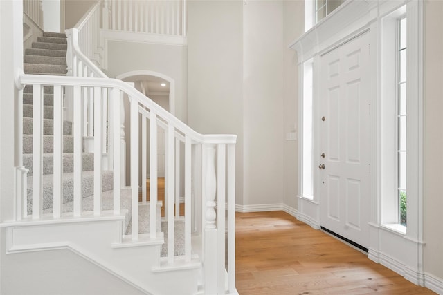 foyer featuring arched walkways, wood finished floors, baseboards, and stairs