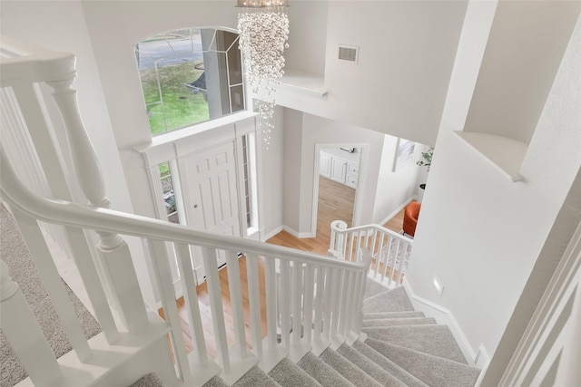 staircase with baseboards, wood finished floors, a towering ceiling, and visible vents