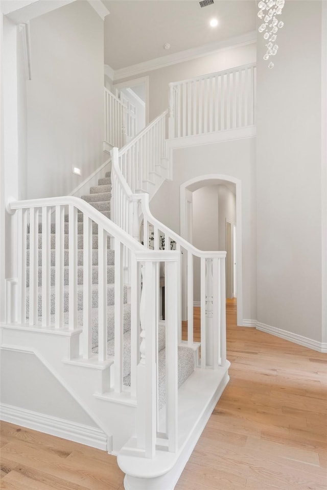 stairs featuring a high ceiling, arched walkways, wood finished floors, and baseboards