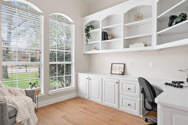 office space featuring plenty of natural light, built in study area, light wood-style floors, and baseboards