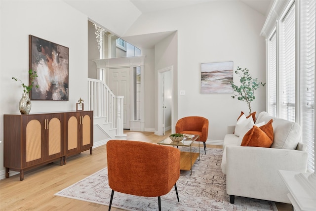 living area featuring high vaulted ceiling, stairway, light wood-style floors, and a healthy amount of sunlight