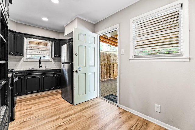 kitchen featuring dark cabinets, ornamental molding, a sink, freestanding refrigerator, and tasteful backsplash