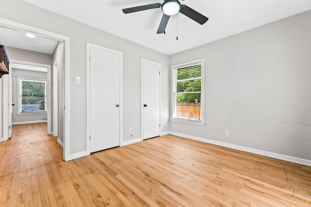 unfurnished bedroom with two closets, baseboards, a ceiling fan, and light wood-style flooring