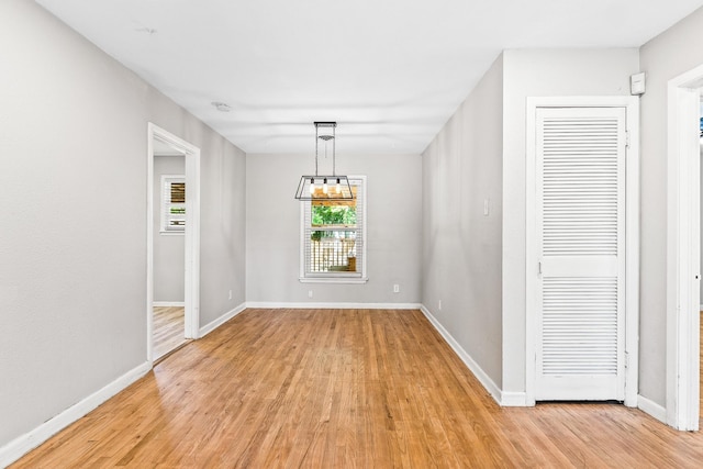 unfurnished dining area featuring light wood-type flooring, baseboards, and a chandelier