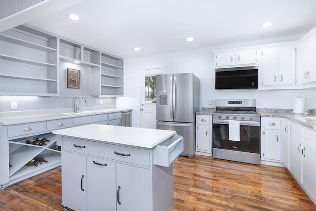 kitchen featuring appliances with stainless steel finishes, open shelves, a sink, light countertops, and wood finished floors