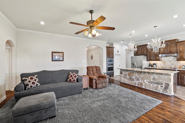 living room with ceiling fan with notable chandelier, dark wood finished floors, arched walkways, ornamental molding, and recessed lighting