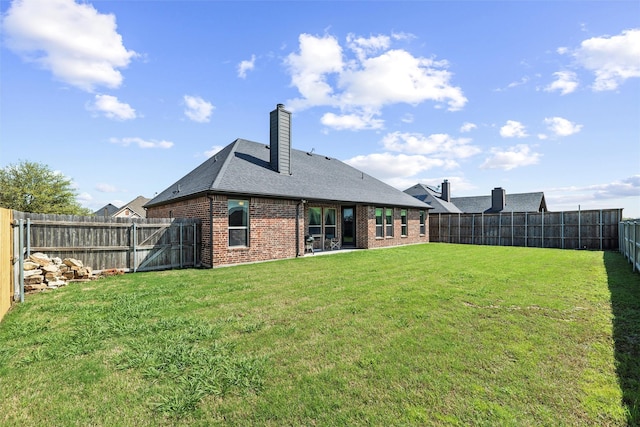 rear view of property with a chimney, a lawn, brick siding, a fenced backyard, and a shingled roof