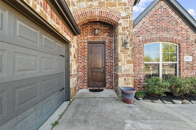 doorway to property featuring a garage, concrete driveway, and brick siding