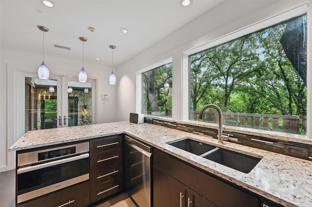 kitchen featuring oven, dark brown cabinetry, light stone countertops, a sink, and visible vents