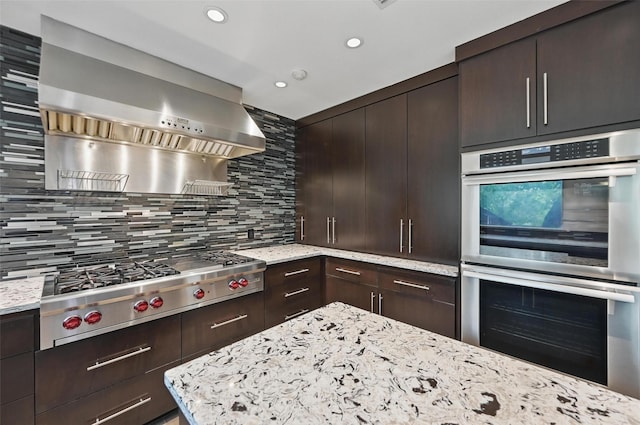 kitchen featuring wall chimney exhaust hood, appliances with stainless steel finishes, backsplash, and dark brown cabinetry