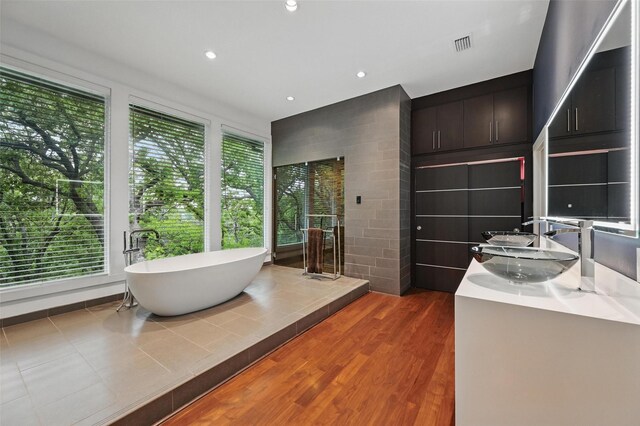 full bathroom featuring double vanity, visible vents, a freestanding tub, wood finished floors, and a sink