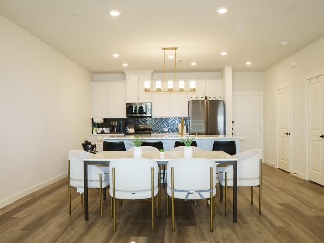 kitchen featuring wood finished floors, an island with sink, decorative backsplash, stainless steel appliances, and baseboards