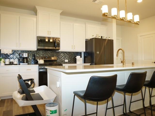 kitchen with tasteful backsplash, a kitchen island with sink, a breakfast bar, stainless steel appliances, and white cabinets