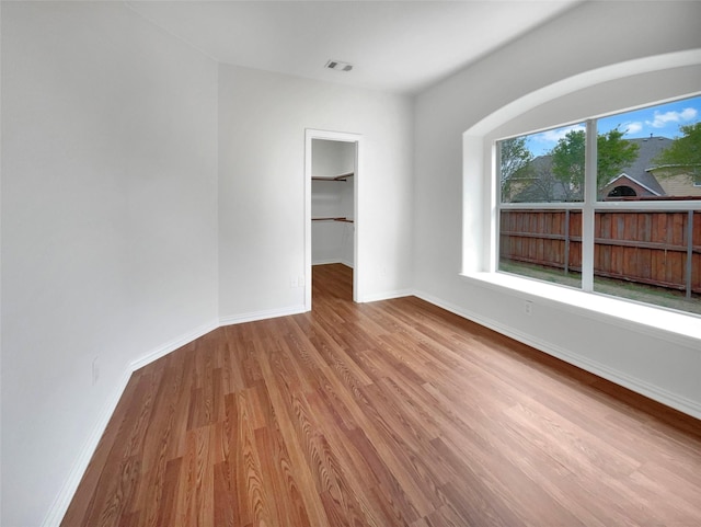 unfurnished bedroom with a spacious closet, visible vents, baseboards, and wood finished floors