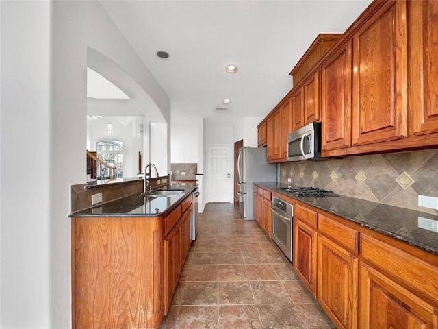 kitchen with tasteful backsplash, dark stone countertops, a sink, brown cabinetry, and stainless steel appliances