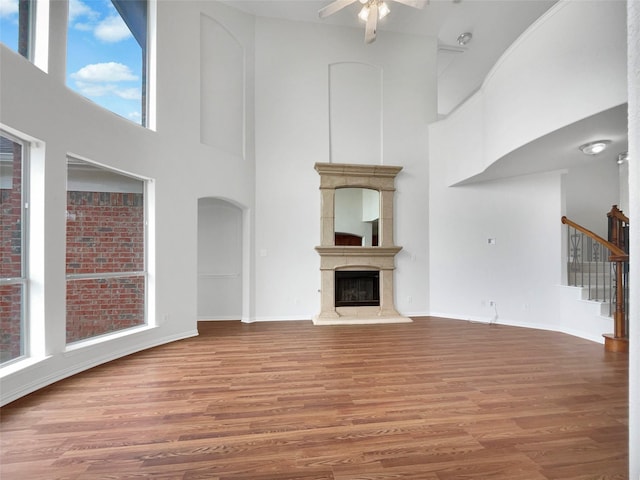 unfurnished living room with ceiling fan, a towering ceiling, wood finished floors, and stairs