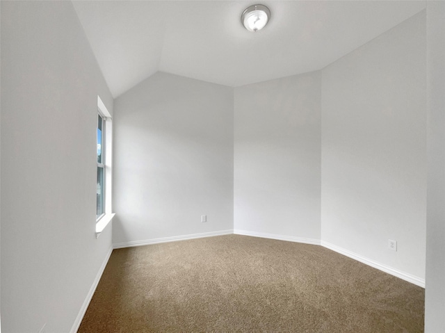 carpeted spare room featuring baseboards and vaulted ceiling