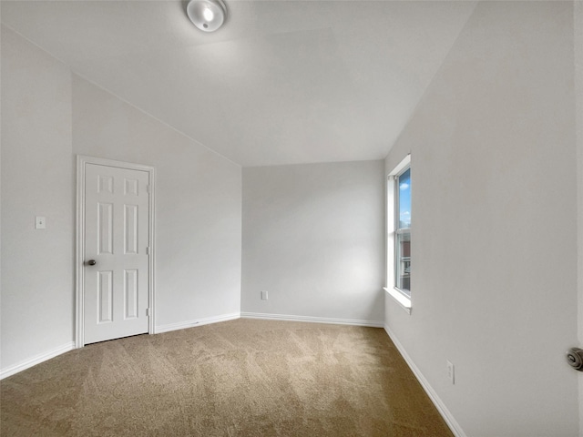 carpeted spare room with baseboards and vaulted ceiling