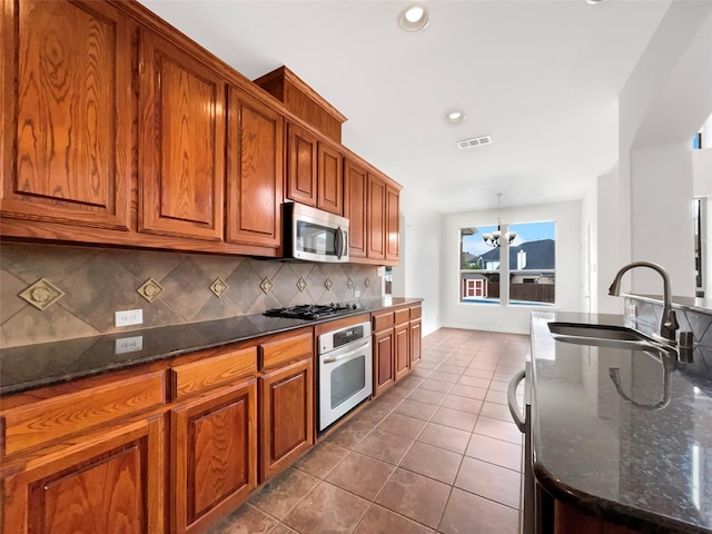 kitchen featuring visible vents, appliances with stainless steel finishes, a sink, dark tile patterned floors, and backsplash
