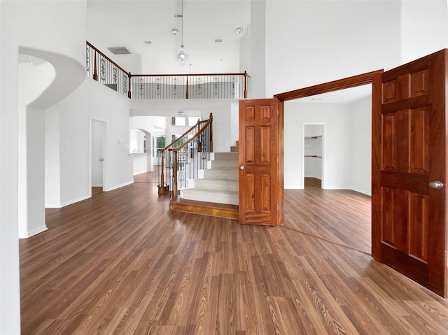 interior space featuring arched walkways, a high ceiling, baseboards, and wood finished floors