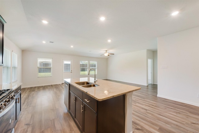 kitchen featuring a sink, light wood-type flooring, open floor plan, dark brown cabinets, and appliances with stainless steel finishes