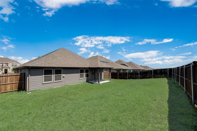 rear view of house with a lawn, a fenced backyard, and roof with shingles