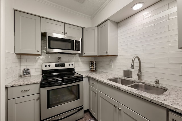 kitchen with ornamental molding, gray cabinets, stainless steel appliances, and a sink