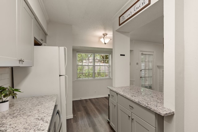 kitchen with dark wood finished floors, baseboards, freestanding refrigerator, light stone countertops, and dishwasher